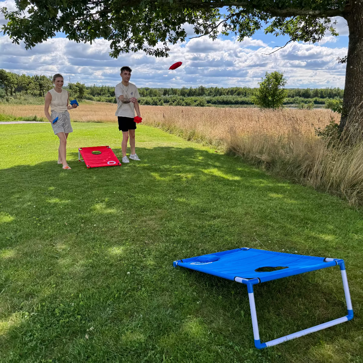 2 personer som spiller cornhole fra cornhole.dk med beach set strandsættet i pvc og stof, med røde og blå ærteposer og cornholeposer