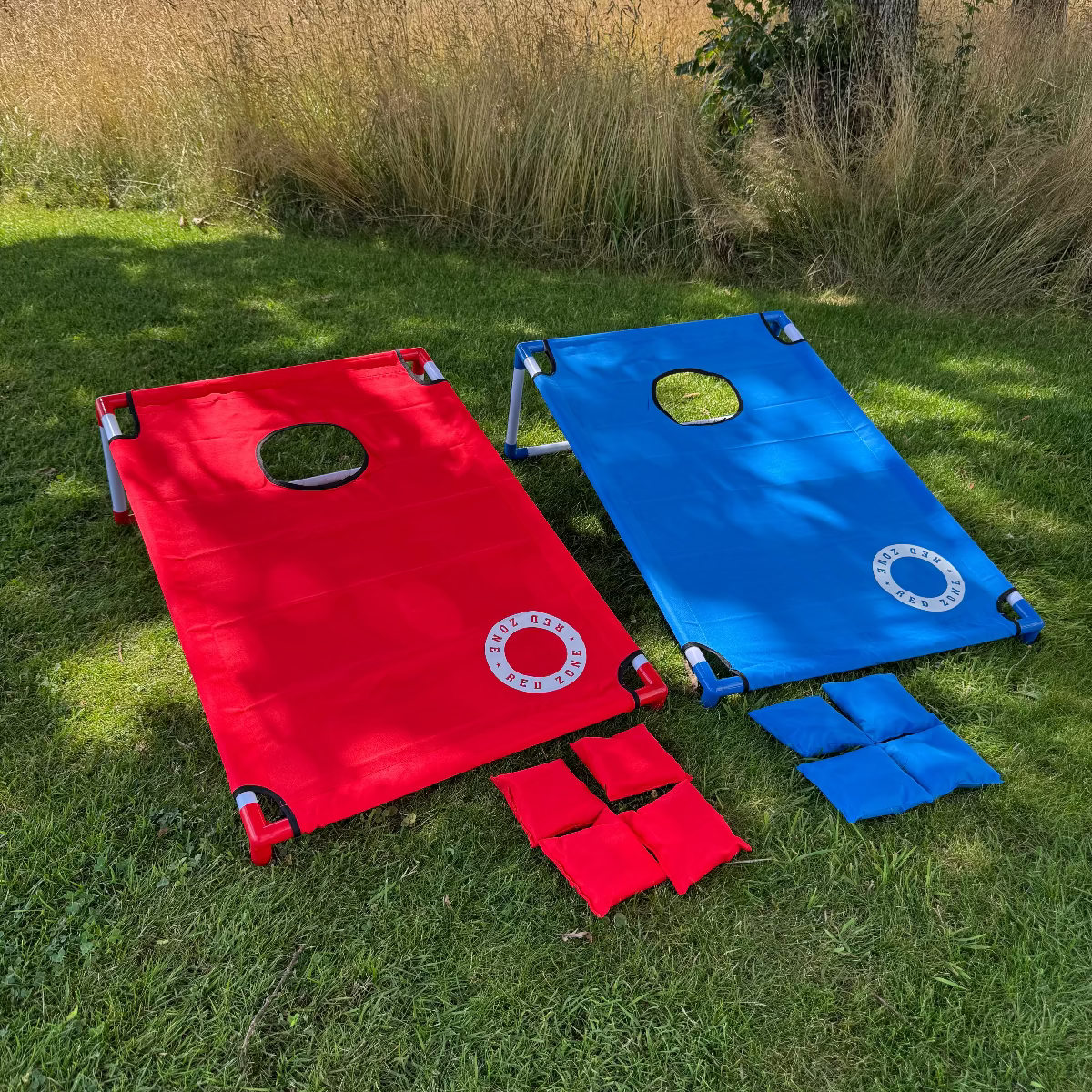 Cornhole strandsæt 2 bræt i rød og blå står på græsset med kasteposer i rød og blå cornholeposer og ærteposer i et ærteposekast spil