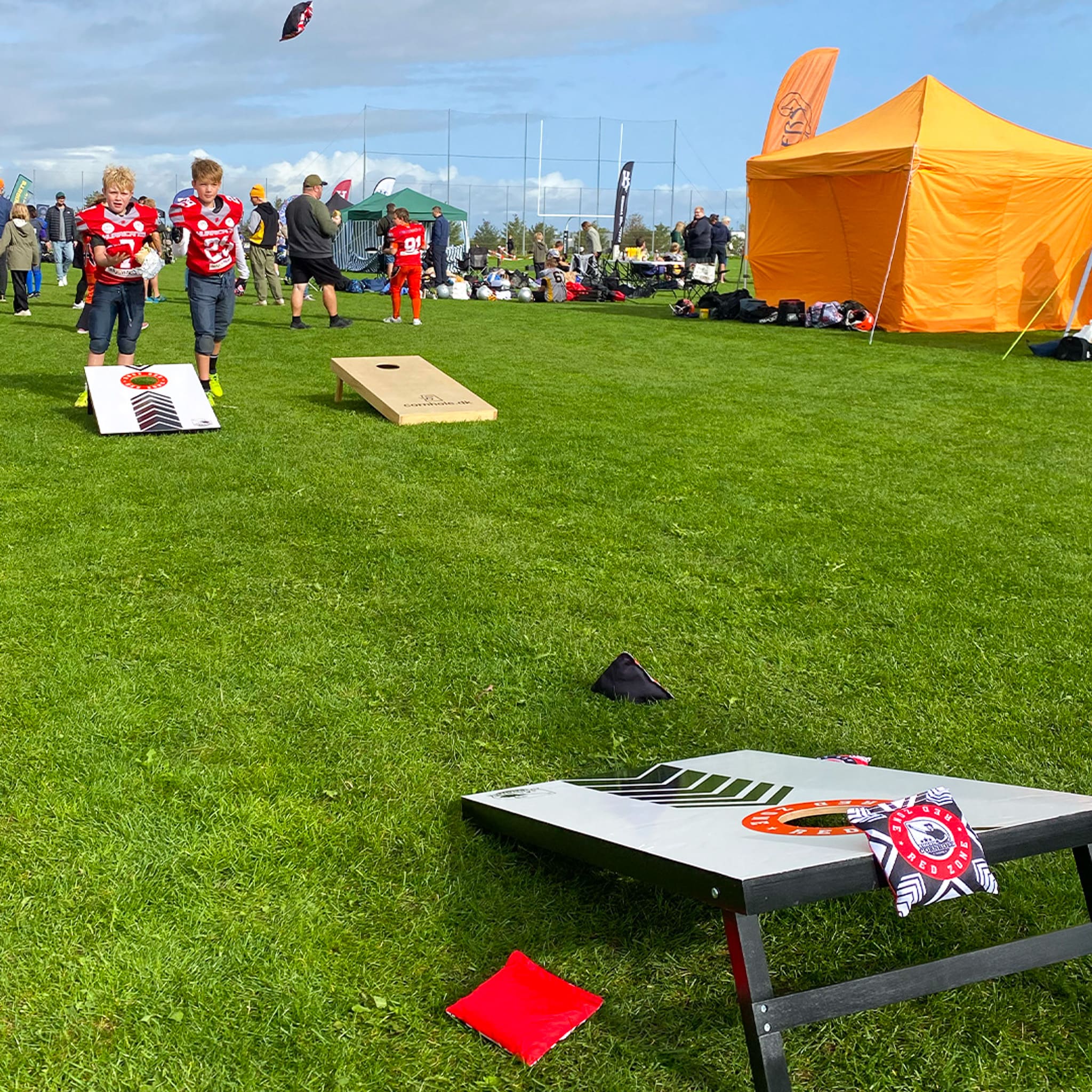 Børn spiller cornhole med redzone cornholesÌt pü en grÌsplÌne iført udstyr til amerikansk fodbold med et orange telt i baggrunden