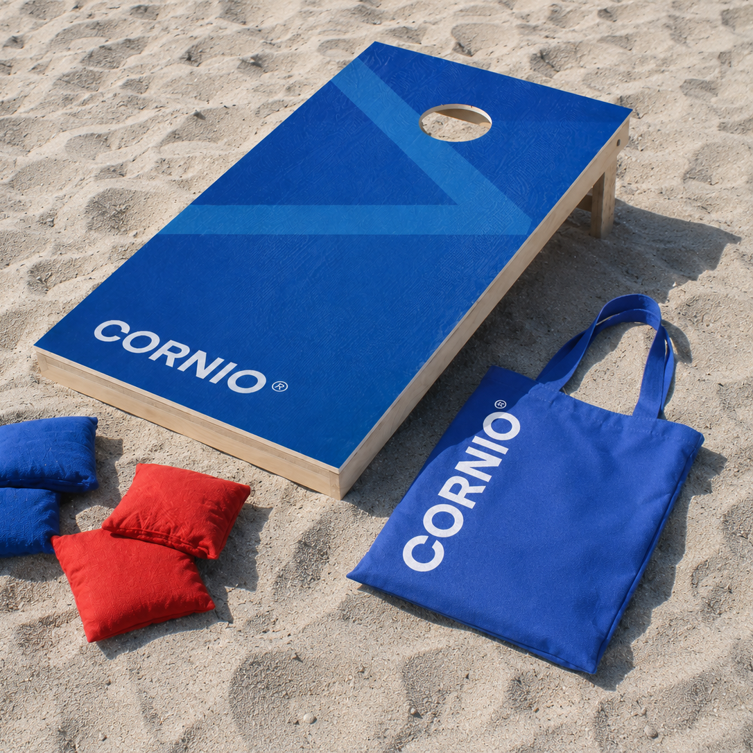 Cornio mulepose på strand med et cornio cornholesæt i træ med blå farve, røde og blå cornholeposer ligger i sandet, blå bommuldskanvas stoffpose til opbevaring og transport af kasteposer