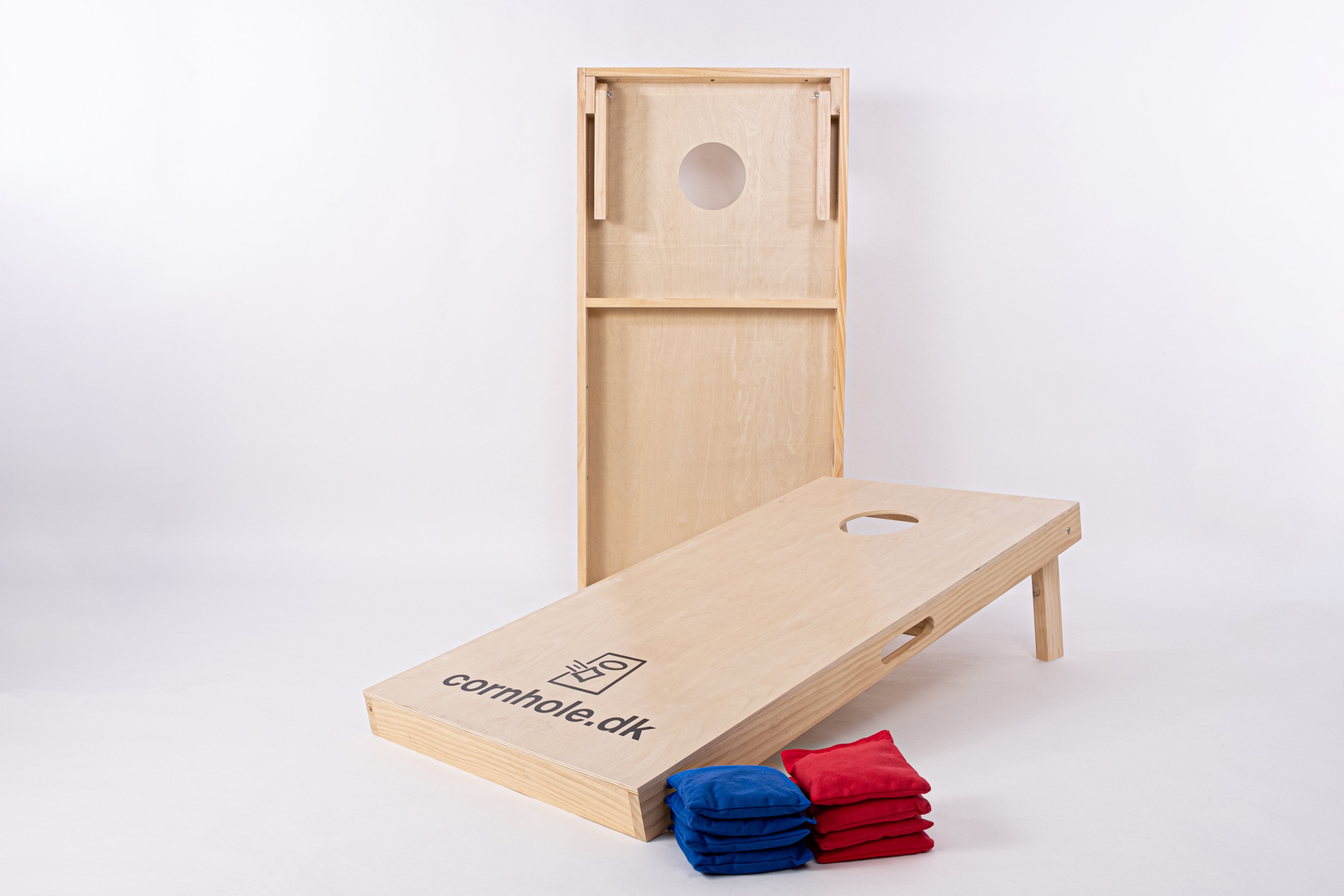 Cornholesæt i de officielle mål 120x60 cm fra cornhole.dk med 8 stk. kasteposer i blå og rød farve. Billedet er taget i et photostudie med god belysning, og man kan se den høje kvalitet og flotte træ. 